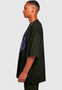 Sort oversized t-shirt med korte ærmer og et livligt lilla grafisk design på forsiden. Blødt bomuldsmateriale, afslappet pasform.
