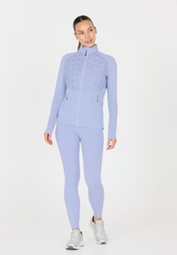 Ljusblå idrottsjacka med vadderad frontpanel, hög krage och dragkedjefickor. Matchad med slanka ljusblå leggings och silverskor.