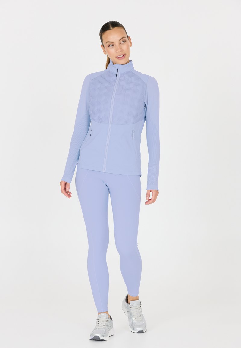 Ljusblå idrottsjacka med vadderad frontpanel, hög krage och dragkedjefickor. Matchad med slanka ljusblå leggings och silverskor.