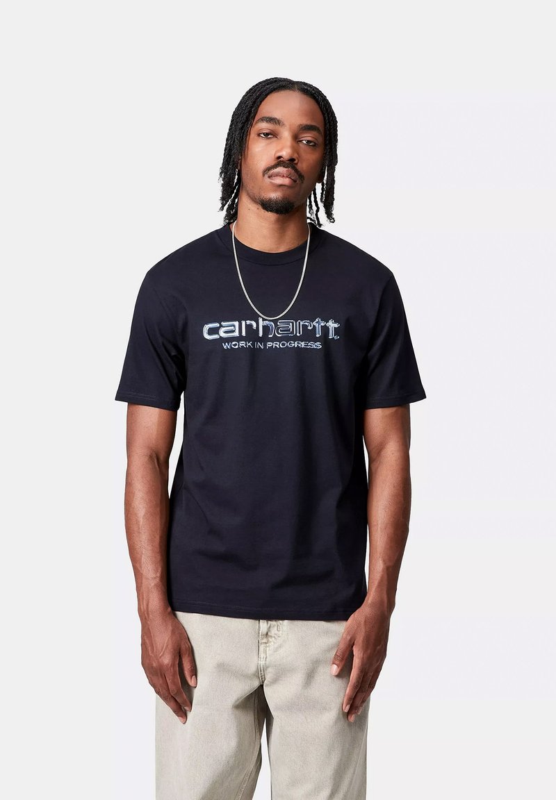 T-shirt in cotone nera con maniche corte e colletto girocollo, caratterizzata da un logo ricamato blu "carhartt" e il testo "WORK IN PROGRESS".