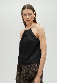 Black sleeveless top made of smooth fabric, featuring a keyhole neckline and a gold-tone accent at the straps.