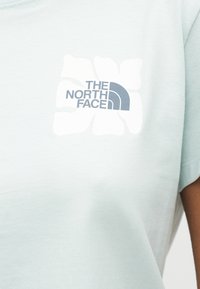 Ανοιχτό μπλε μπλουζάκι με λευκό λουλούδι ιβίσκου και μπλε λογότυπο "The North Face" τυπωμένο στο στήθος.