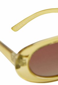 Geltonos saulės akiniai su blizgančiais rėmeliais, rudais lęšiais ir tiesiomis rėlėmis. Ant rėlės yra užrašas „MADE IN CHINA“ ir CE ženklai.