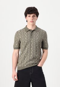 Polo en maille vert olive avec manches courtes, présentant un motif géométrique, une patte de boutonnage à trois boutons, ainsi que des poignets et un ourlet côtelés.