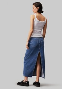 Denim maksi krilo z visokim razporkom, srednje modra pranja in dvema zadnjima žepoma. V kombinaciji z belo majico brez rokavov in črnimi platformnimi čevlji.