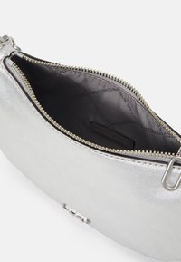 Clutch argentato con zip, finitura metallica e superficie texturizzata, che rivela un interno in tessuto scuro con foderatura logo.