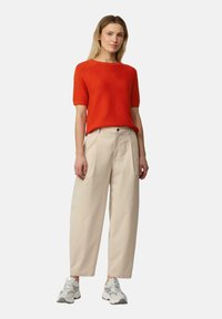 Rode gebreide trui met korte mouwen, gecombineerd met beige wide-leg broek en grijze sneakers. De outfit heeft een ontspannen pasvorm en een eenvoudig ontwerp.
