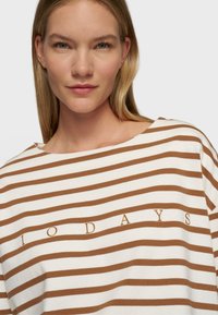 Bruine en witte gestreepte oversized t-shirt met een bootnek. "10 DAYS" in bruine letters op de voorkant gedrukt. Zachte katoenen stof.