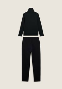 Top de cuello alto negro de manga larga y pantalones negros a juego dispuestos sobre un fondo neutro.