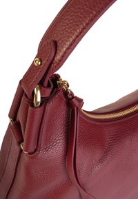 Bolso de cuero burdeos con un acabado texturizado, que presenta un zipper y herrajes dorados, una forma curvada y una correa gruesa para llevar.
