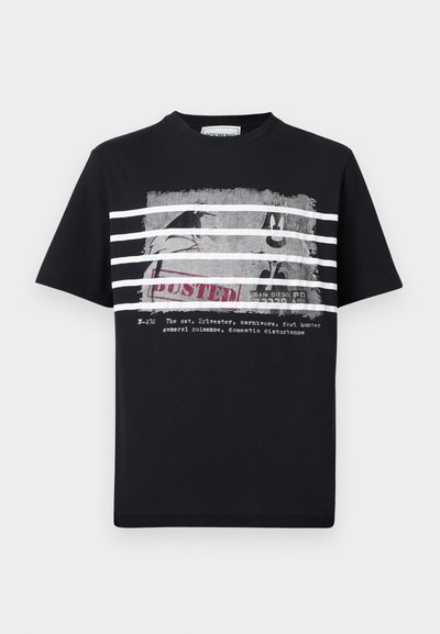 T-shirt noir avec des rayures blanches sur un graphisme en noir et blanc du personnage de dessin animé Sylvester derrière des barreaux, avec le mot « BUSTED » et un texte en dessous.