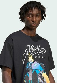 Ung mand iført en sort oversized t-shirt med et farverigt grafik af et skelet i brand, der kører på en motorcykel, samt fed typografi.