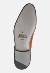 Suola di scarpa in pelle marrone con sezioni in gomma grigia, caratterizzata dal marchio inciso "HENRY STEVENS" e piccoli chiodi metallici per migliorare la trazione.