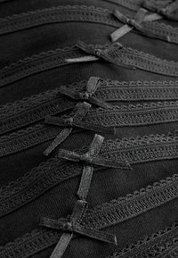 Black textile featuring layered rows of decorative black lace trim and small bows, creating a textured and intricate surface design.