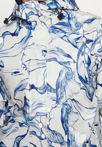 Chaqueta resistente al agua en blanco con un atrevido patrón floral abstracto en azul, capucha ajustable con cordón y cierre frontal de cremallera.