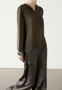 Chemise manches longues vert olive avec un col henley, une légère brillance et une texture douce. Associée à un pantalon satiné ample assorti.