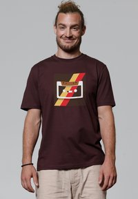 Bordeaux katoenen t-shirt met een retro cassettebandje grafiek en gele en rode strepen. Korte mouwen, ronde halslijn, ontspannen pasvorm.