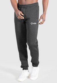 Graue Jogginghosen mit einem elastischen Bund, seitlichen Taschen und weißen Logodetails. Getragen mit weißen Sportschuhen.