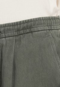 Buks i bomuldsblanding i en dæmpet grøn nuance, med en tekstureret stof, diskrete folder og en struktureret talje.