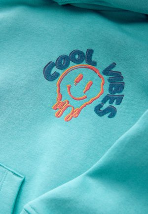 Hanorac turcoaz cu textură moale, având inscripția „Cool Vibes” și un grafic cu față zâmbitoare brodat în portocaliu și albastru.
