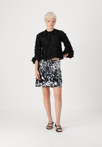 Μαύρο cropped top με υφασμάτινη υφή και μακριά μανίκια, συνδυασμένο με φανταχτερή ασημί μίνι φούστα επενδυμένη με στρας. Μαύρες σαγιονάρες ολοκληρώνουν την εμφάνιση.