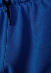 Gros plan sur un pantalon de survêtement en tissu bleu avec taille élastique et cordon noir.