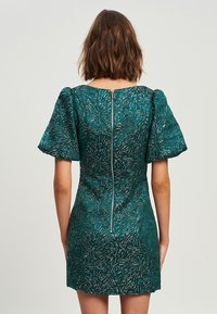 Vestido verde con estampado, con mangas cortas abullonadas, diseño ajustado y cremallera en la parte trasera central. La tela tiene un estampado texturizado similar a hojas.