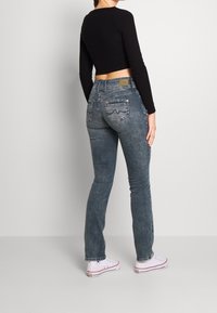 Top corto de manga larga negro combinado con jeans ajustados grises. Los jeans cuentan con bolsillos traseros con costura decorativa. El modelo lleva zapatillas blancas.