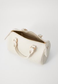 Sac à main en cuir texturé blanc avec quincaillerie dorée, double poignées et fermeture éclair. L'intérieur est ouvert avec un détail de poche unique.