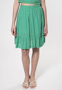 Falda verde bordada con dobladillo festoneado, cinturilla elástica y detalles de volantes. Tejido ligero con patrones de ojales en todo.