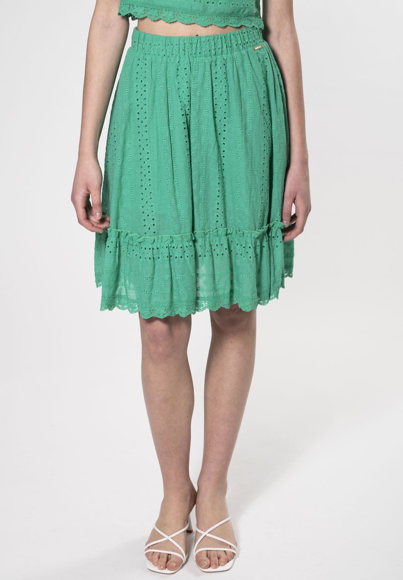 Falda verde bordada con dobladillo festoneado, cinturilla elástica y detalles de volantes. Tejido ligero con patrones de ojales en todo.