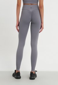 Leggings texturate gri cu talie înaltă, având un model geometric, țesătură elastică și o siluetă elegantă. Se poartă cu încălțări negre.