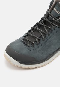 Grijze suède wandelschoen met rubberen teenkap, gaasdetails en reflecterende veters. Heeft een gestructureerde bovenkant en een lichtgekleurde, duurzame zool.