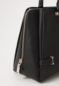 Black textured handbag featuring a gold zipper, structured shape, and a side buckle detail for secure closure.