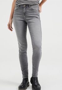 šedé skinny džíny s jemnou texturou, obsahující pět kapes, zapínání na knoflík a kontrastní černé boční pruhy. Nanaseny s černými botami.