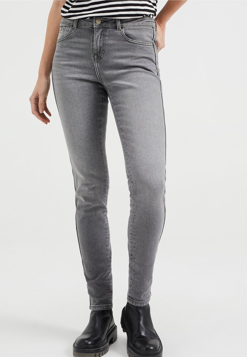 šedé skinny džíny s jemnou texturou, obsahující pět kapes, zapínání na knoflík a kontrastní černé boční pruhy. Nanaseny s černými botami.