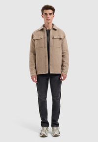Beige wollen blend jasje met een kraag, twee voorzakken en knoopsluiting. Gecombineerd met donkere spijkerbroeken en gestreepte sneakers.