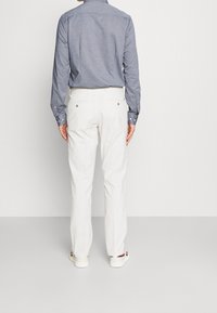 Camisa de manga larga azul con cuello tipo button-down, combinada con pantalones blancos y zapatillas blancas informales. Tejido texturizado, diseño ajustado.