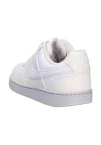 Sneaker bianca in pelle con superficie testurizzata, suola grigia e colletto imbottito. Presenta un sottile logo Nike sul tallone e una chiusura con lacci.