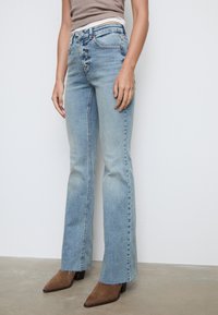 Jeans svasati blu chiaro in denim con una finitura sbiadita, caratterizzati da una vita alta, design a cinque tasche e orlo sfilacciato alle caviglie.