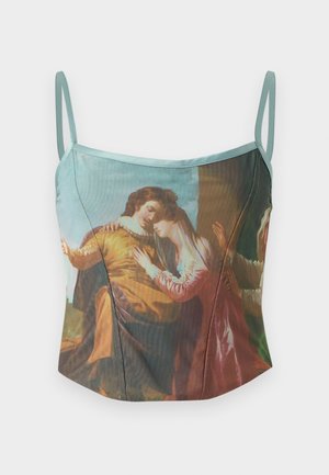 Žena s dlhými tmavými vlasmi, ktorá má na sebe potlačený top na špagety a široké béžové nohavice s vysokým pásom, stojaca s rukami v vreckách.