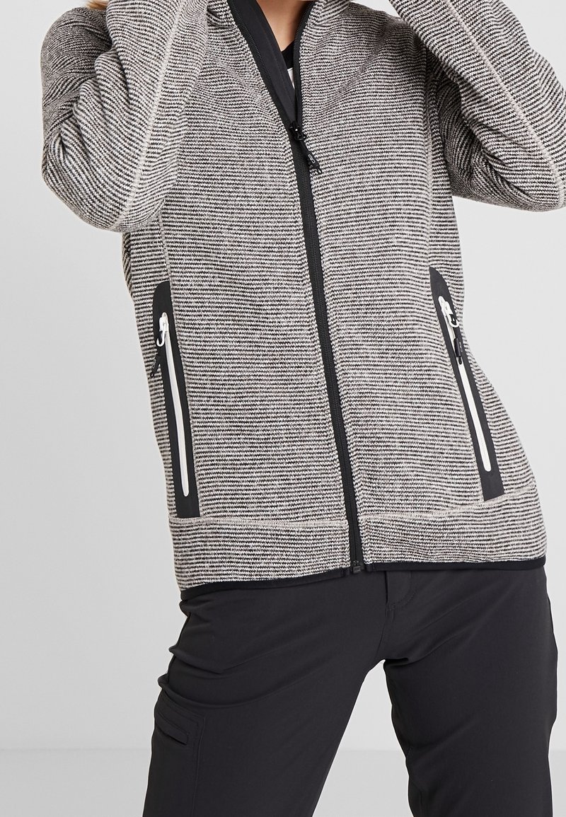 Veste zippée rayée noire et grise avec un col haut, poches latérales zippées et une finition texturée. Accents noirs mats au bas et aux poignets.