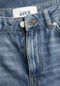 Jeans in denim blu con chiusura tradizionale a cerniera e bottone, caratterizzati da cuciture arancioni in contrasto e un'etichetta tessuta con la scritta "JJXX."