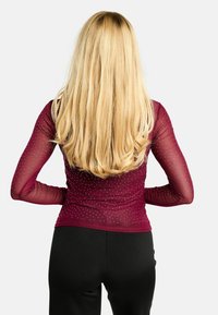 Bordowa bluzka z długim rękawem wykonana z przezroczystej siateczki, ozdobiona małymi cyrkoniami, w połączeniu z czarnymi spodniami. Widok tyłu stroju.