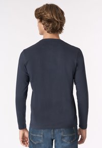 Maglietta a maniche lunghe blu navy con colletto rotondo, texture liscia e design aderente. Abbinata a jeans blu con tasche posteriori.