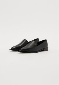 Zapatillas de piel negra sin cordones con punta afilada y un diseño minimalista, que cuentan con un tacón plano y una textura suave.