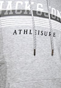 Felpa grigia realizzata in tessuto morbido, con la scritta "JACK & JONES" e "ATHLEISURE" in nero, cordini decorati e punte metalliche.