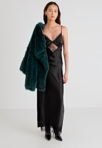 Μαύρο σατέν φόρεμα με λεπτομέρειες δαντέλας, συνδυασμένο με σκούρο πράσινο κασμίρι μπολερό. Το σύνολο ολοκληρώνουν μαύρες μυτερές γόβες.