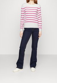 Maglione a righe bianco con strisce rosa, abbinato a jeans svasati blu scuro. Le sneakers bianche completano l'outfit. Design e vestibilità semplici.