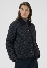 Quilted black jacket with a corduroy collar, front button closure, and side pockets. Fabric has a smooth texture and diamond pattern.